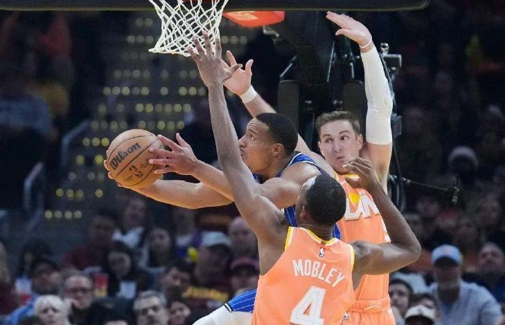 Orlando Magic guard Desmond Bane, left, goes to the basket between Cleveland Cavaliers center Evan Mobley (4) and guard Sam Merrill, right, in the first half of Tuesday's game in Cleveland.